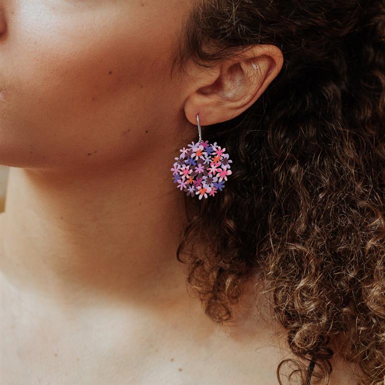 Close-up of a person wearing colorful floral earrings with curly hair.