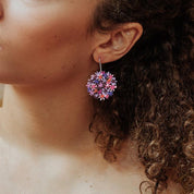 Close-up of a person wearing colorful floral earrings with curly hair.