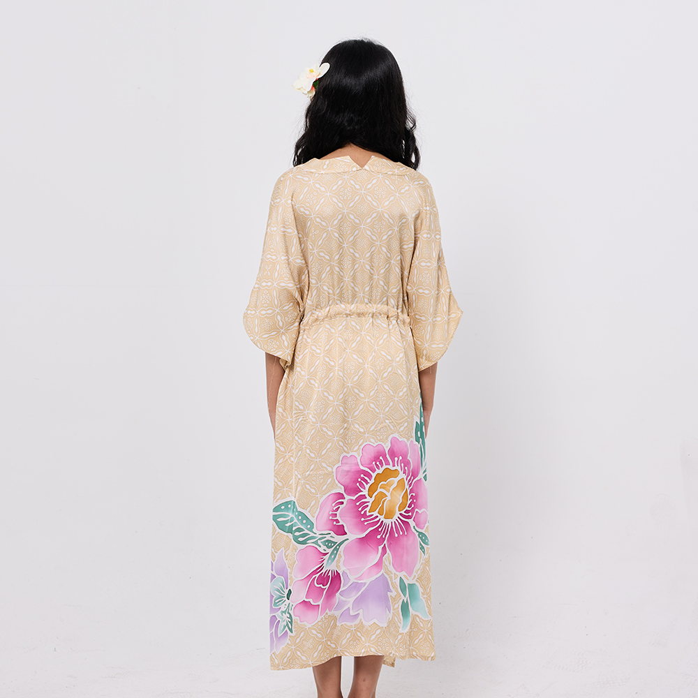 Woman wearing a beige floral dress with a pink flower design on a plain background