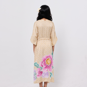 Woman wearing a beige floral dress with a pink flower design on a plain background