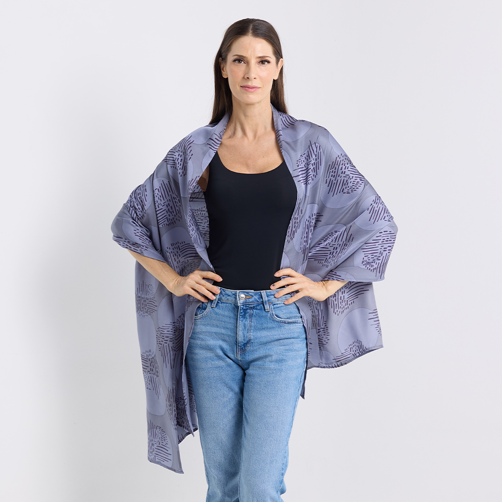 Woman wearing a patterned kimono over a black top and blue jeans on a white background