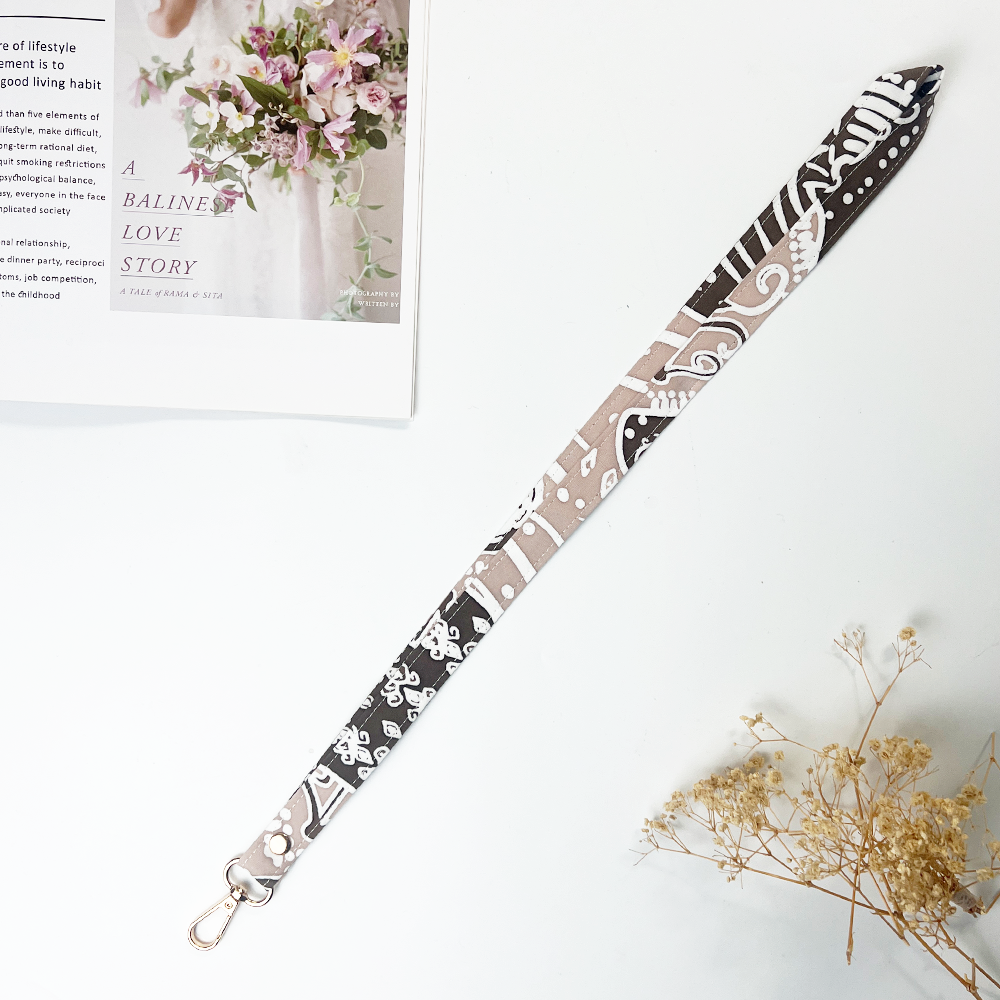Decorative lanyard with floral pattern on a white surface with flowers and text in the background