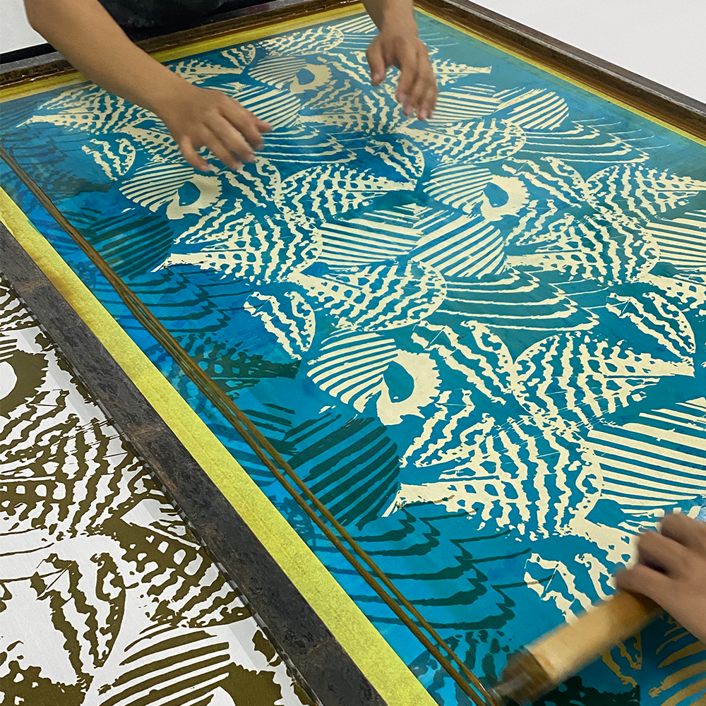Screen printing process with a person using a squeegee on a screen with shell designs.