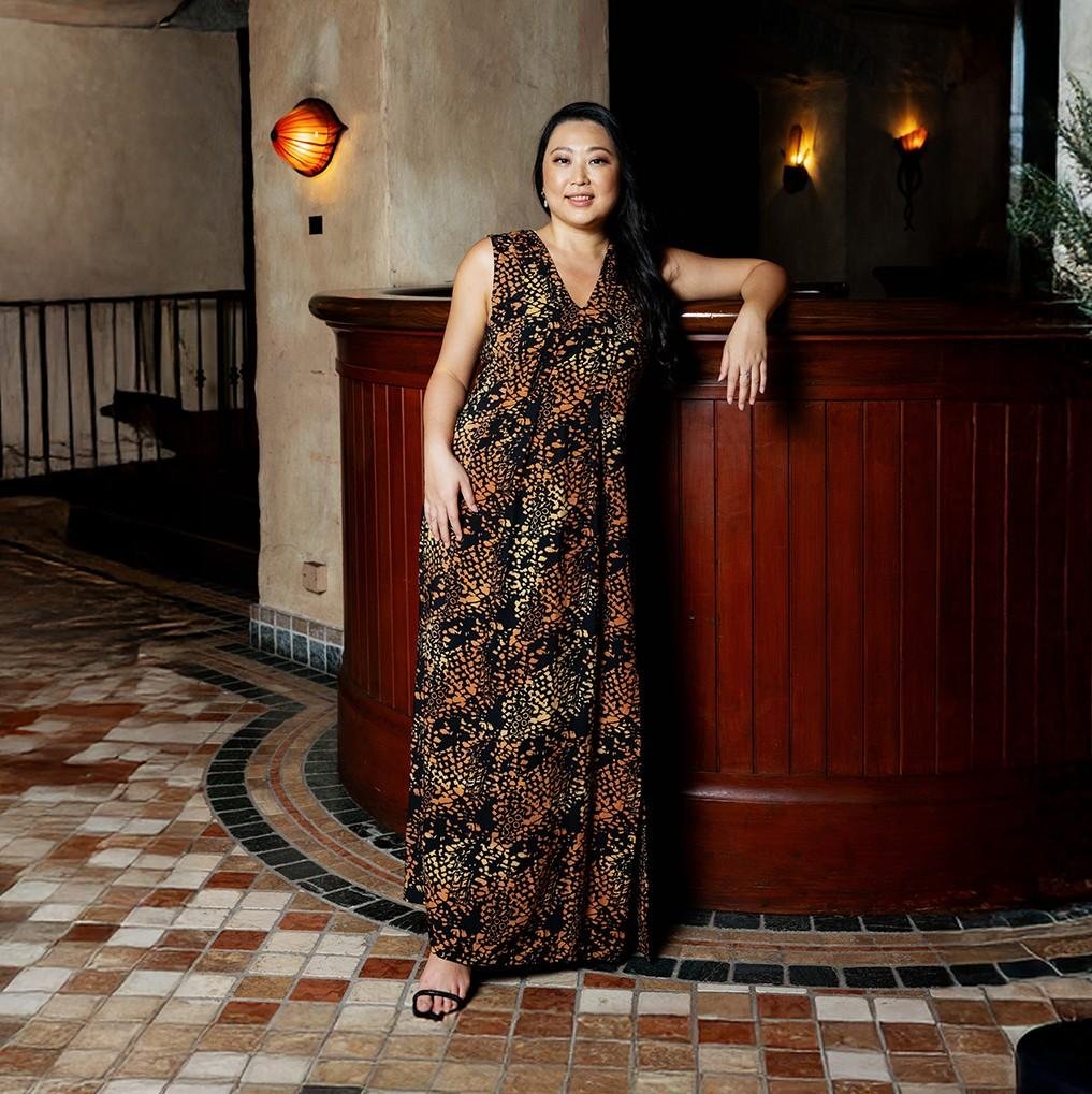 Woman in a patterned dress standing in an elegant interior setting.