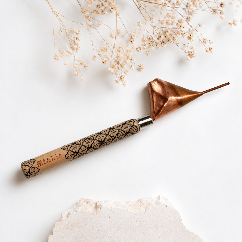 A hand tool with a copper-colored metal tip and a patterned wooden handle, photographed on a white surface with dried flowers and a stone prop.