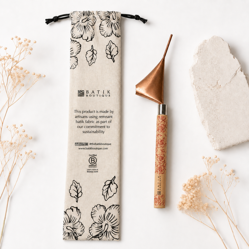 A flat-lay product photograph of a Batik Boutique bamboo-handled scraper tool next to its printed canvas drawstring pouch, styled with dried flowers and a stone on a white background.