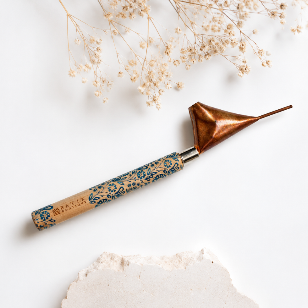A hand tool with a copper-colored metal tip and a patterned wooden handle, styled on a white background with dried flowers and a piece of textured paper.