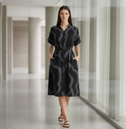 Woman wearing a black patterned dress standing in a modern indoor setting.