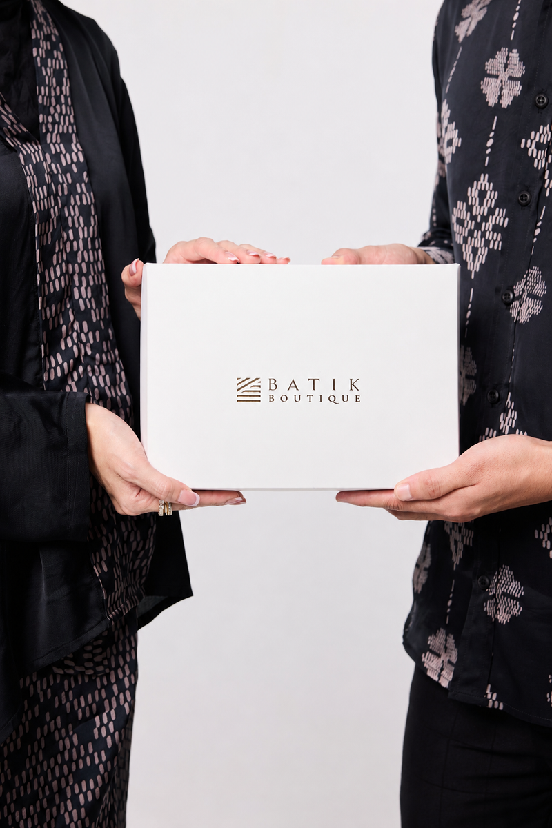 Two people holding a white box with 'Batik Boutique' branding against a plain background.