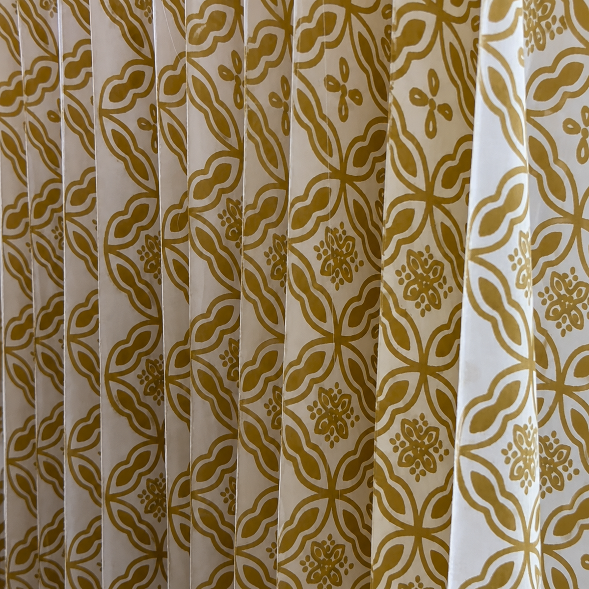 Close-up of pleated curtains with a repeating geometric and floral pattern in mustard yellow on an off-white background.