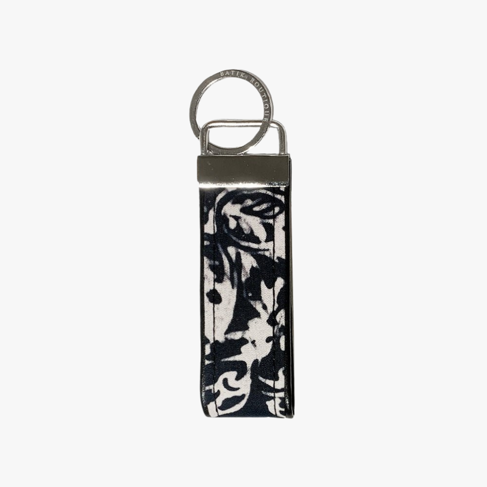 A rectangular leather keychain strap with a black and white abstract floral print, attached to a silver metal split ring and keeper.