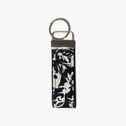 A rectangular leather keychain strap with a black and white abstract floral print, attached to a silver metal split ring and keeper.