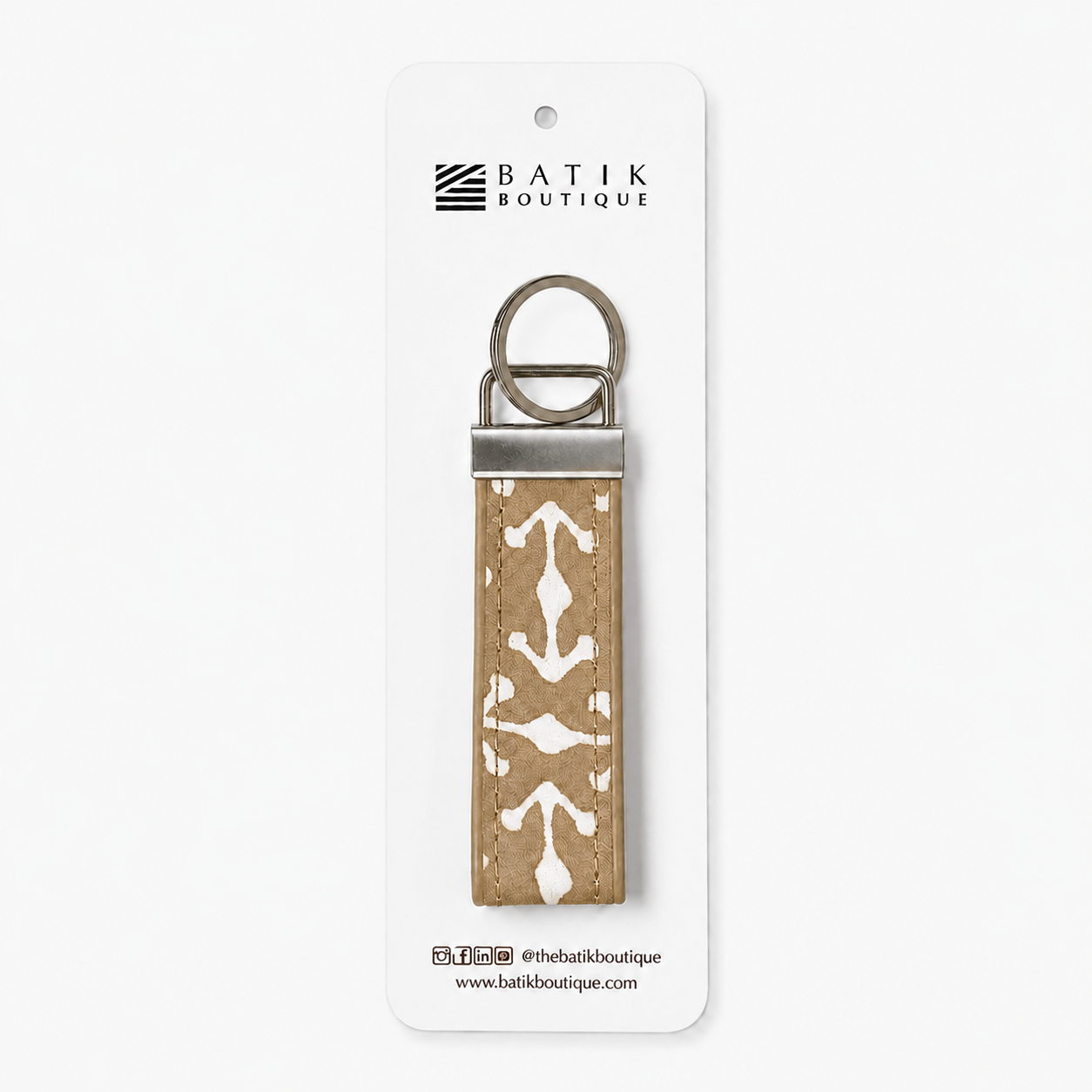 A Batik Boutique keychain with a tan and white batik patterned fabric strap and silver metal hardware, displayed on its white retail card.