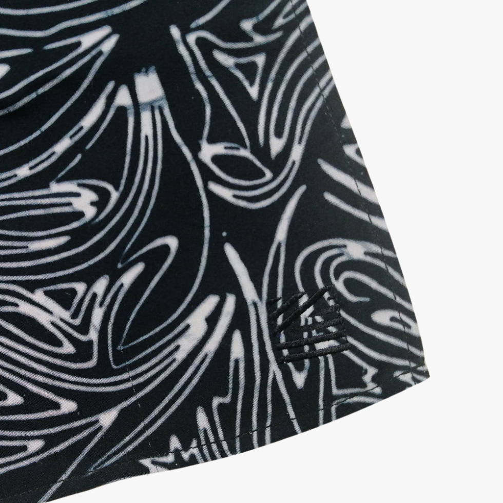 Close-up of a dark gray athletic fabric with a subtle diamond pattern and a small tonal logo patch near the hem, shown on a light gray background.