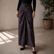 Person wearing a patterned skirt standing in a room with a plant in the background