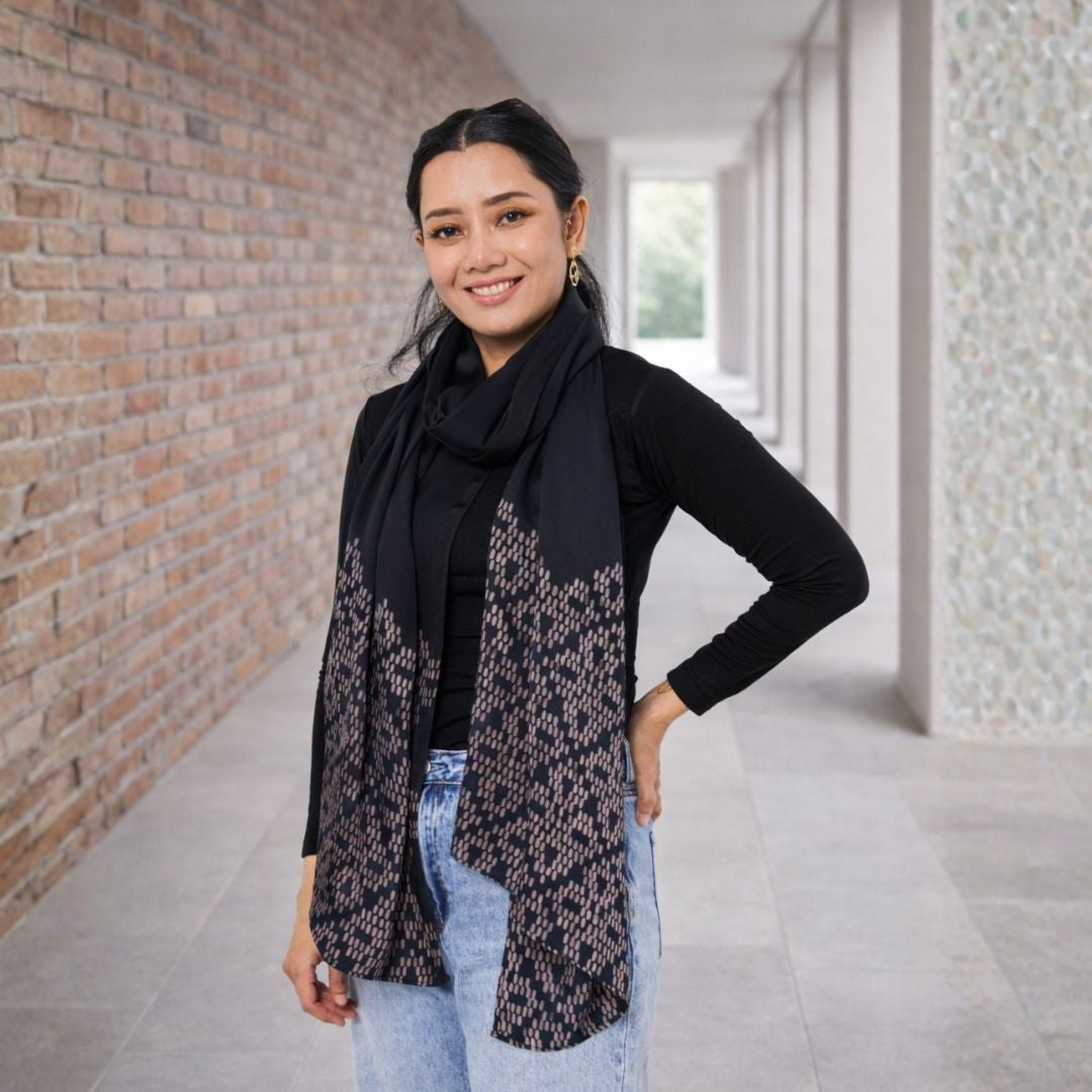 Woman wearing a black scarf with a patterned design in an indoor setting.