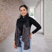Woman wearing a black scarf with a patterned design in an indoor setting.
