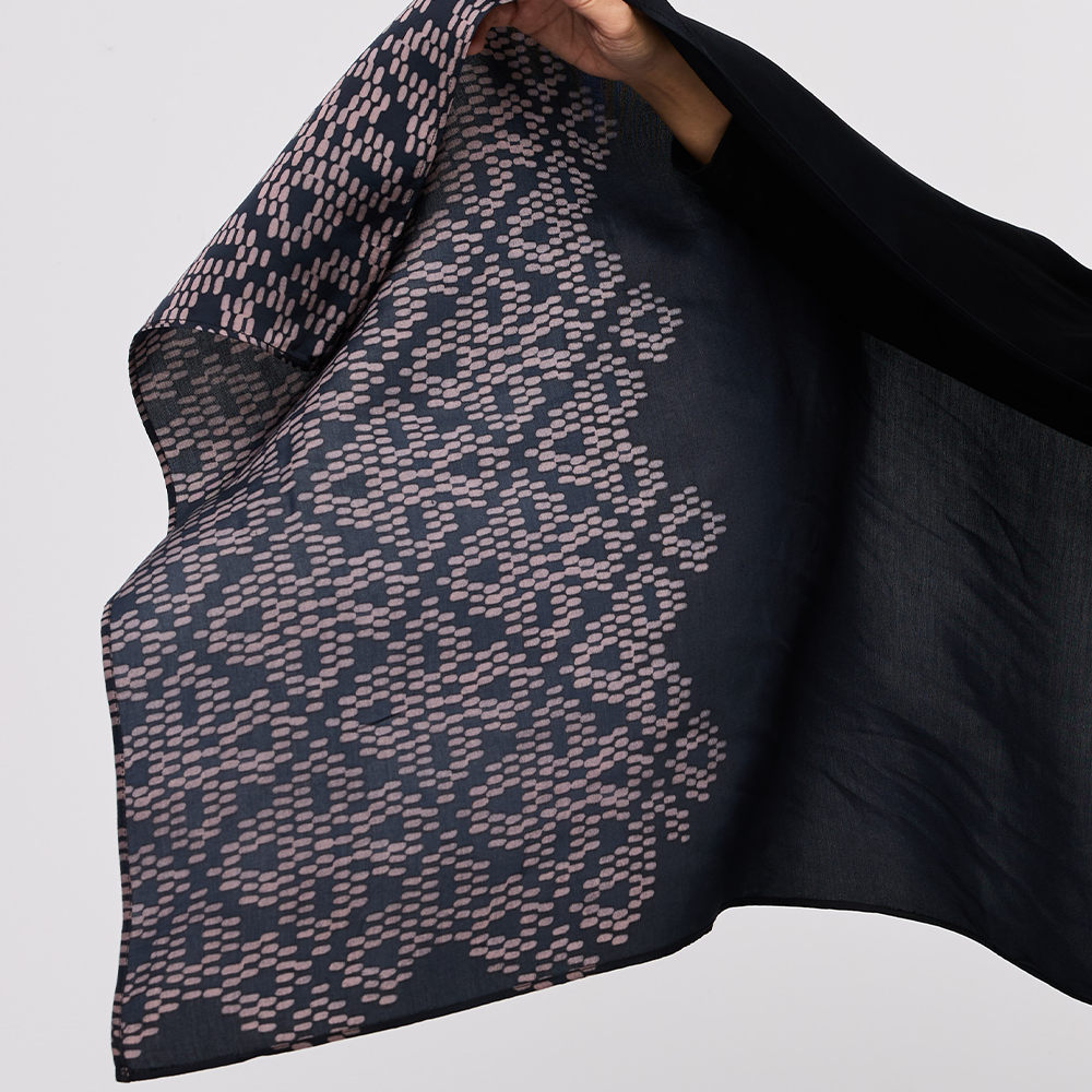 Black and patterned scarf being held against a light gray background