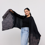 Woman holding a black patterned shawl against a plain background