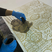 Person applying gold paint to a decorative surface with intricate patterns
