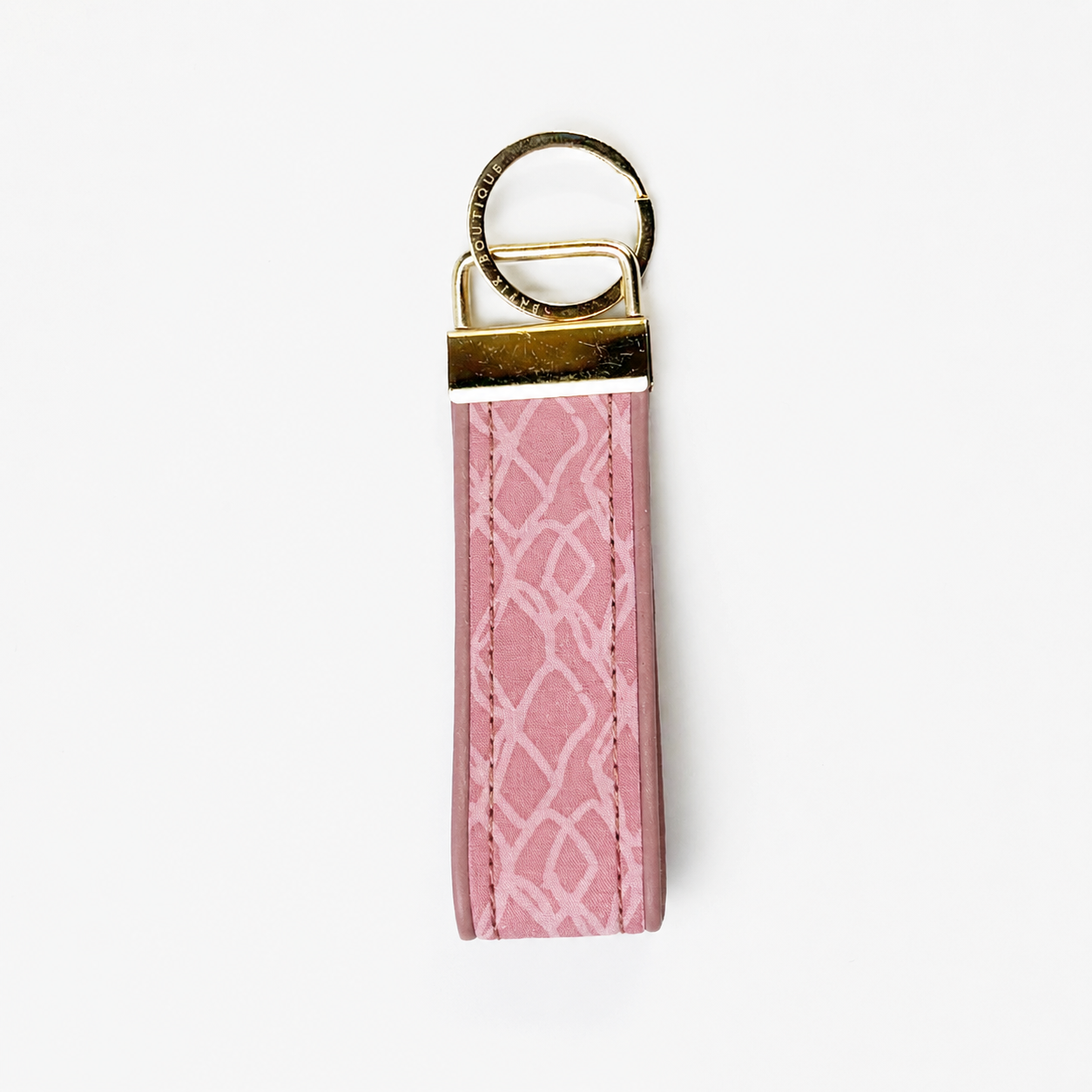 A pink leather keychain featuring a white geometric trellis pattern, finished with a gold-tone metal cap and a split key ring, shown on a plain white background.