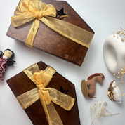 Two wooden gift boxes with gold ribbons on a white surface with decorative items.