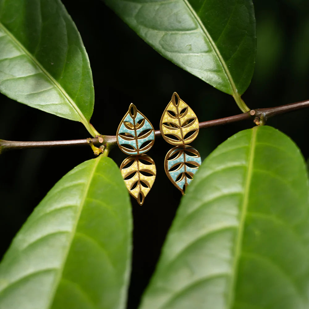 Gold and turquoise leaf-shaped earrings on a branch with green leaves.