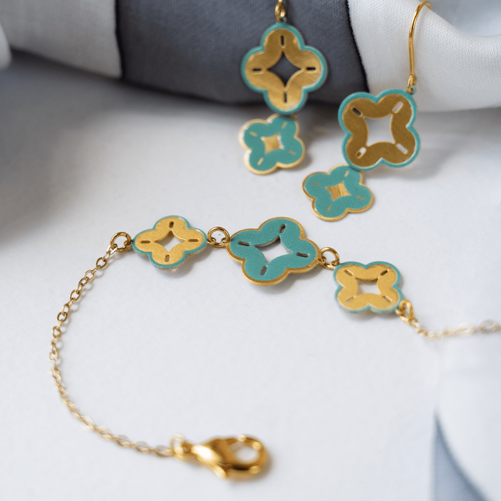 Flat lay of turquoise and gold floral charm bracelet with matching earrings on white fabric.