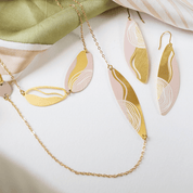 Flat lay of matching batik-inspired earrings and necklace in matte gold and pink on a fabric backdrop.