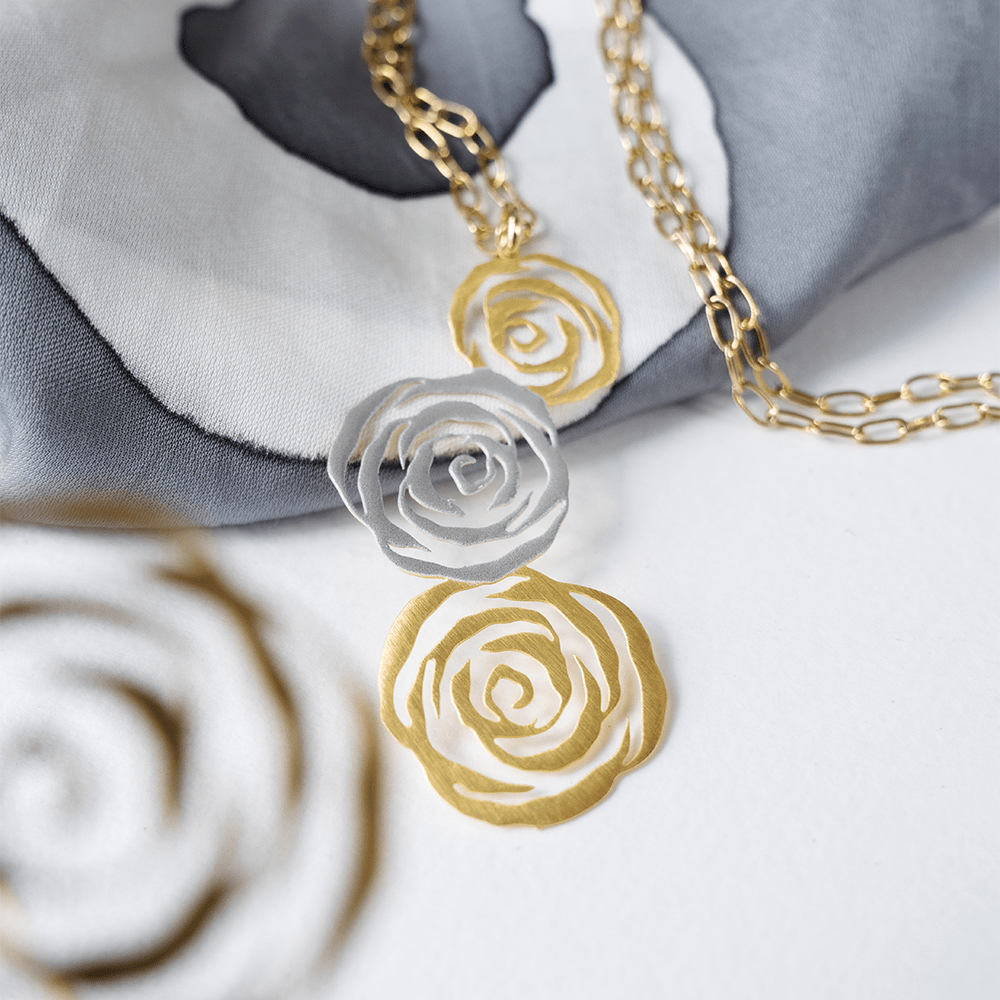 Gold and silver rose-shaped pendants on a soft fabric background