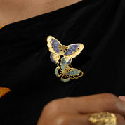 Gold butterfly brooch on a black garment with a hand holding a matching ring.