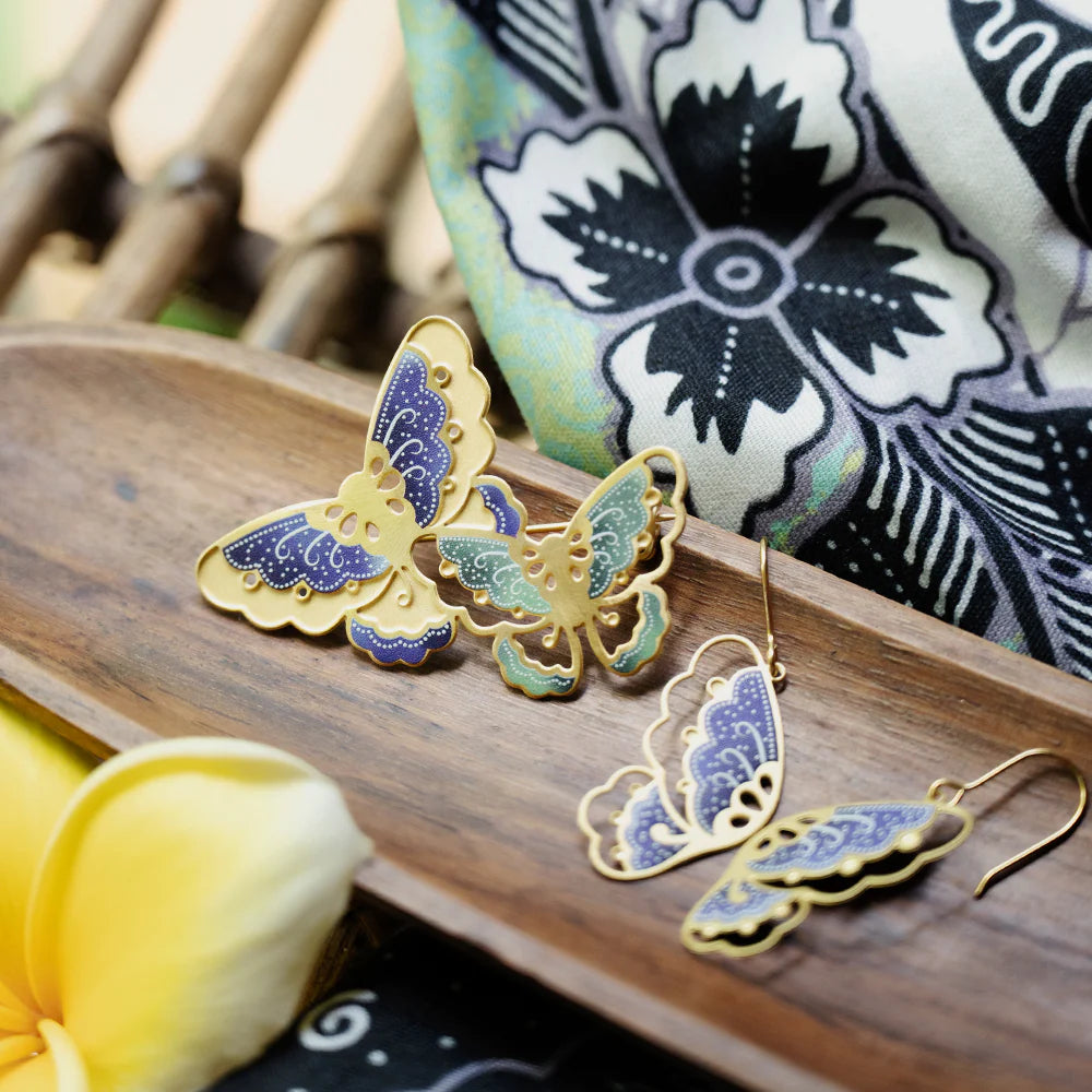 Butterfly-shaped earrings on a wooden surface with a floral patterned fabric in the background.