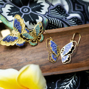 Butterfly-shaped earrings on a wooden surface with a floral pattern in the background