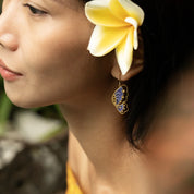 Close-up of a woman wearing butterfly earrings with a blurred natural background