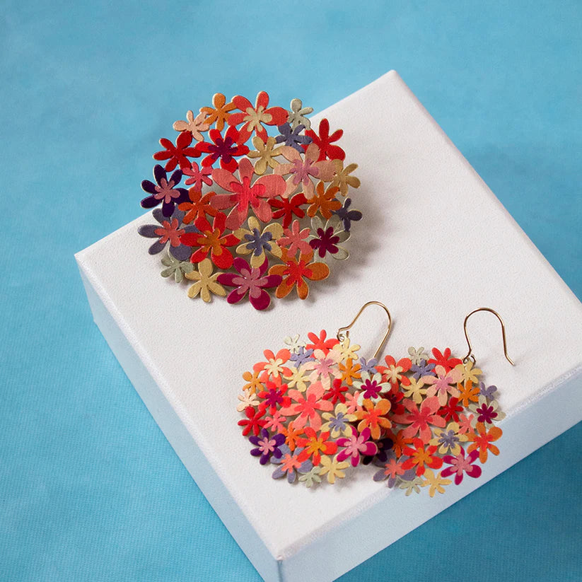Colorful flower-shaped earrings on a white box with a blue background
