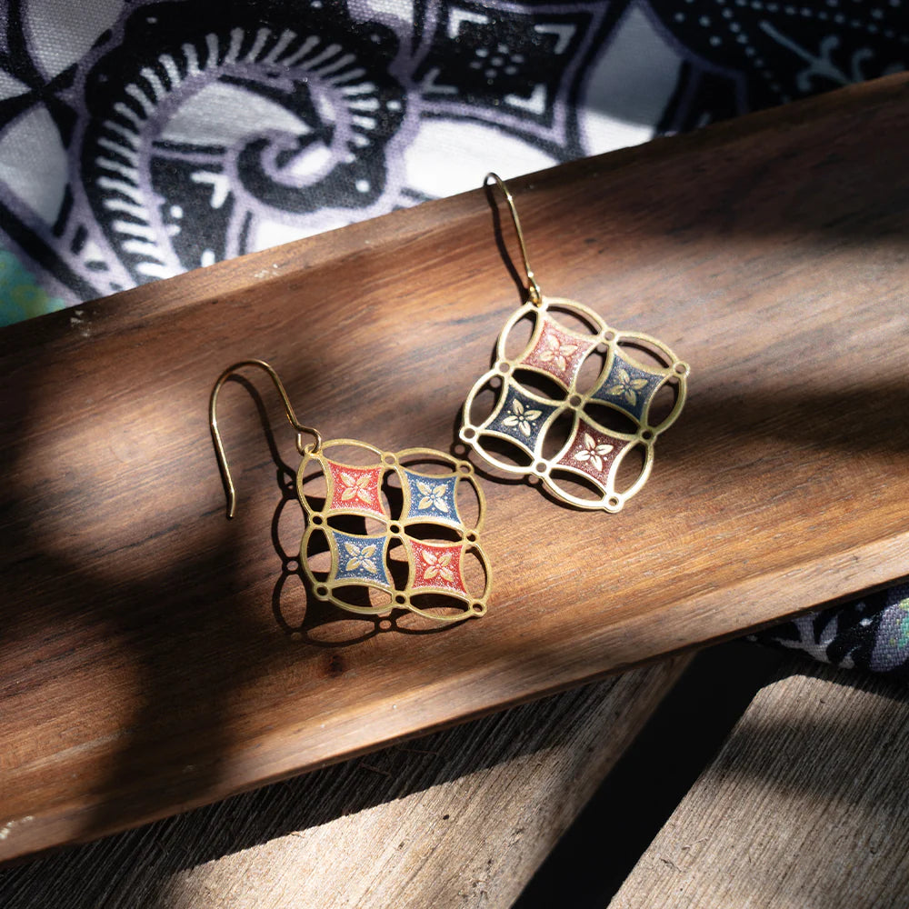 Pair of gold earrings with colorful square designs on a wooden surface