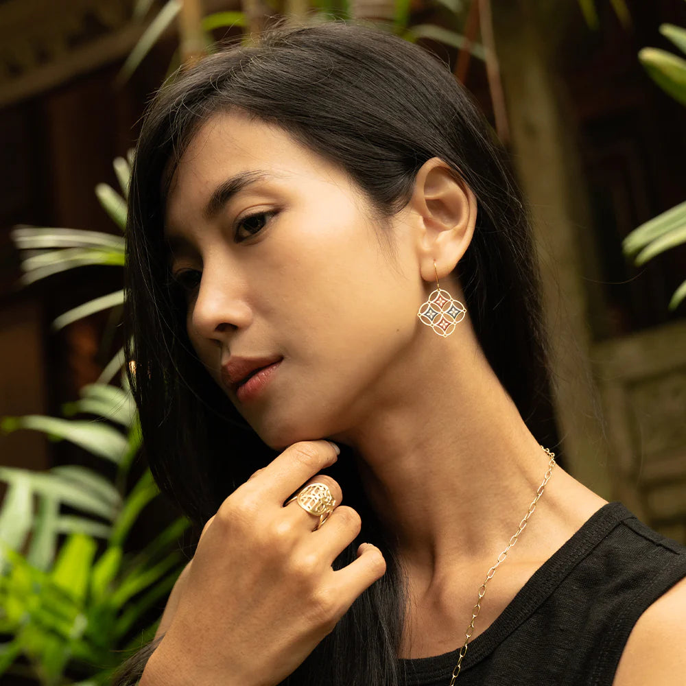 Woman wearing gold earrings and ring with a blurred natural background