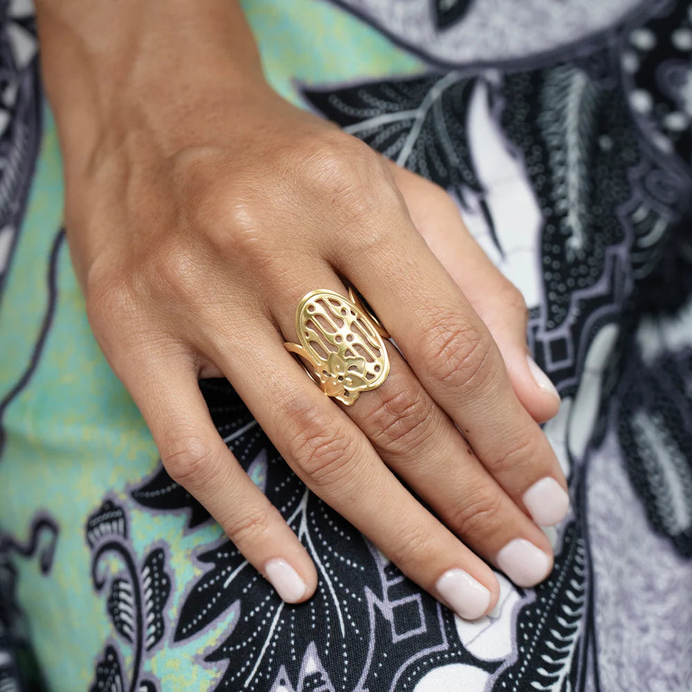 Hand wearing a gold ring with intricate design on a patterned fabric background