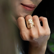 Close-up of a hand wearing a gold ring with a floral design.