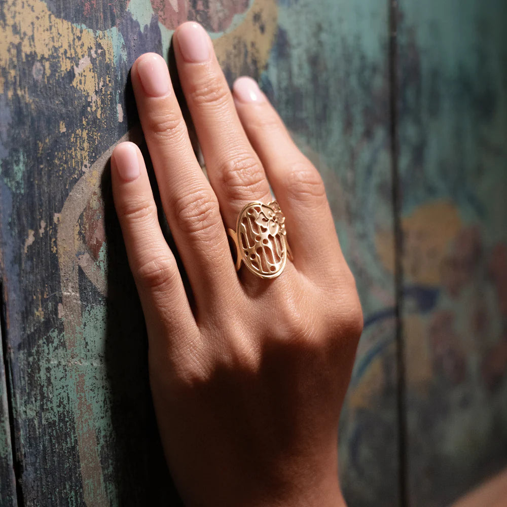 Hand wearing a gold ring against a textured wall