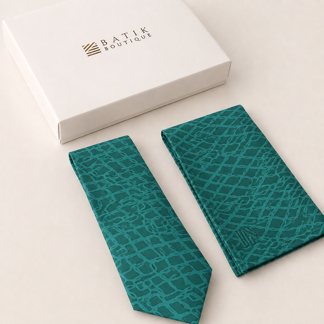 A teal and green batik tie and matching pocket square set with a white gift box from Batik Boutique, displayed on a light beige background.