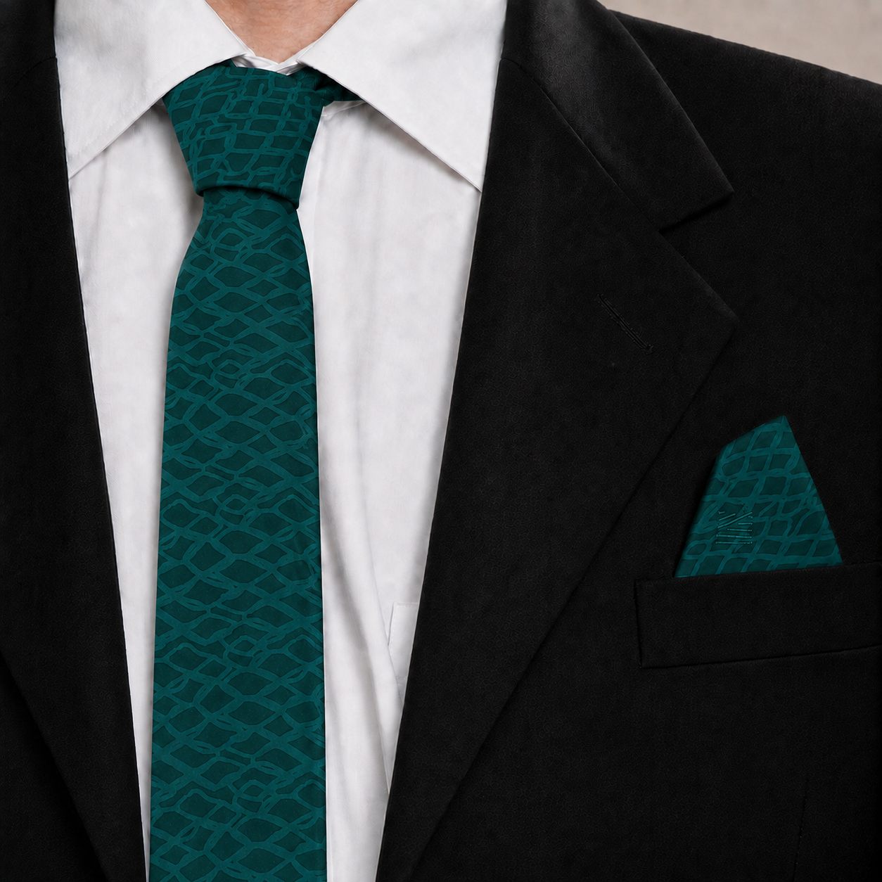 A close-up of a men's formal outfit featuring a dark green patterned silk tie and matching pocket square, styled with a white dress shirt and a black suit jacket.