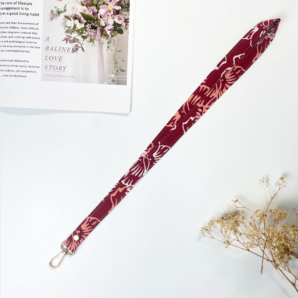 Maroon lanyard with floral pattern on a white surface with a magazine and flowers.
