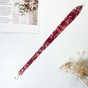 Maroon lanyard with floral pattern on a white surface with a magazine and flowers.