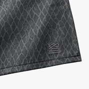 Close-up of a dark gray athletic fabric with a subtle diamond pattern and a small tonal logo patch near the hem, shown on a light gray background.