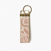 A rectangular keychain or key tag with a dusty pink and white patterned strap, finished with brass-toned metal hardware and a split key ring, shown on a plain white background. Showing the back