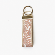 A rectangular keychain or key tag with a dusty pink and white patterned strap, finished with brass-toned metal hardware and a split key ring, shown on a plain white background.