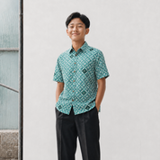 Person wearing a green patterned shirt standing against a light gray wall.
