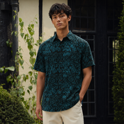 Man wearing blue and black printed batik shirt, posing outdoors with a hand in a pocket