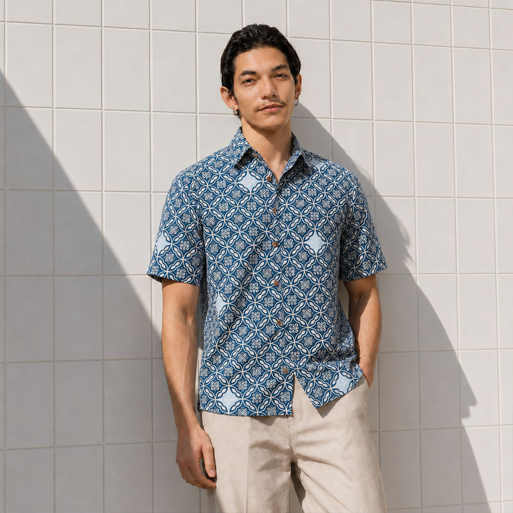 Man wearing blue printed batik shirt, posing by the wall outside with his hand in his pocket